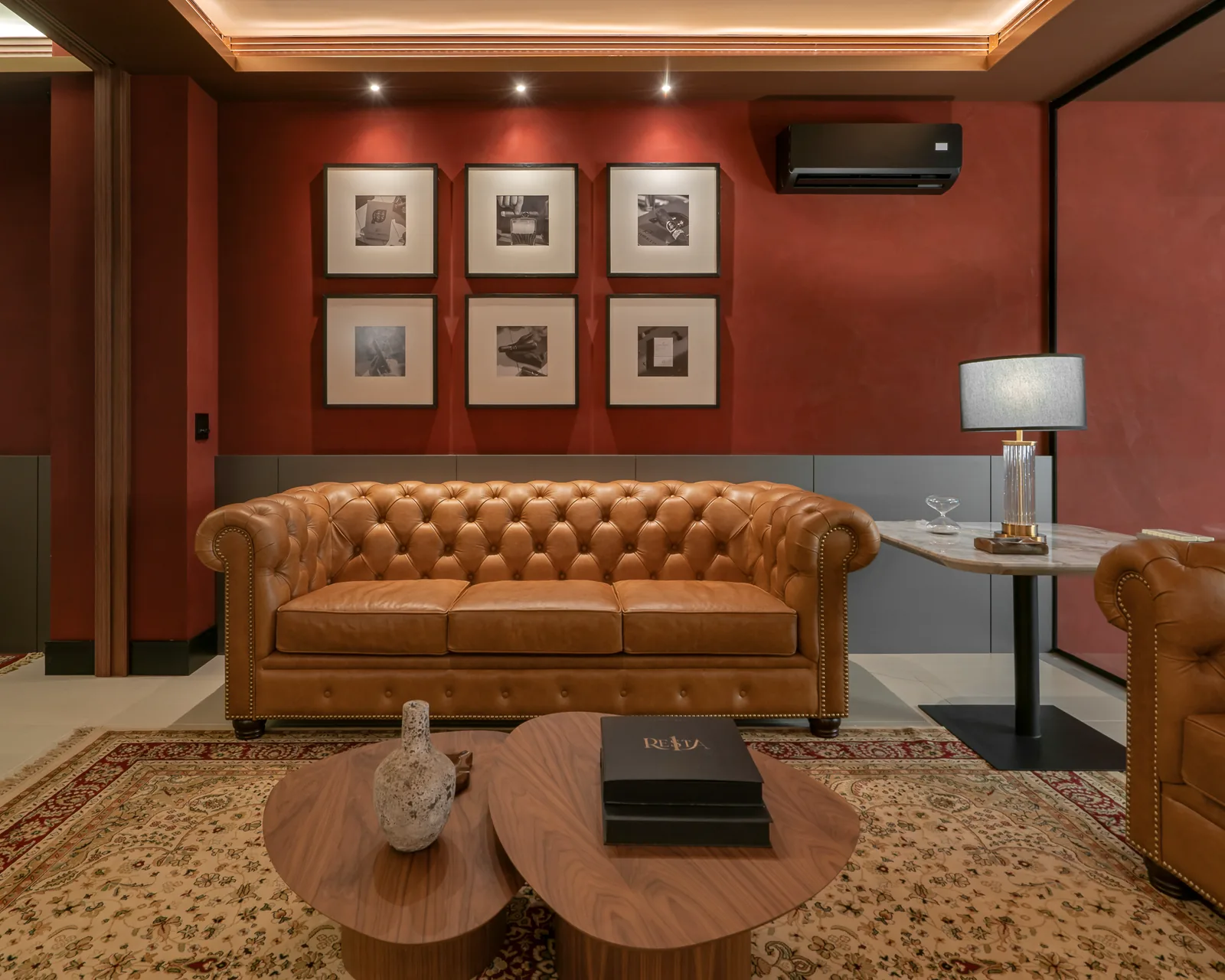 Sala da Gran Tobacco com sofá Chesterfield de couro caramelo, parede terracota, quadros emoldurados e tapete persa