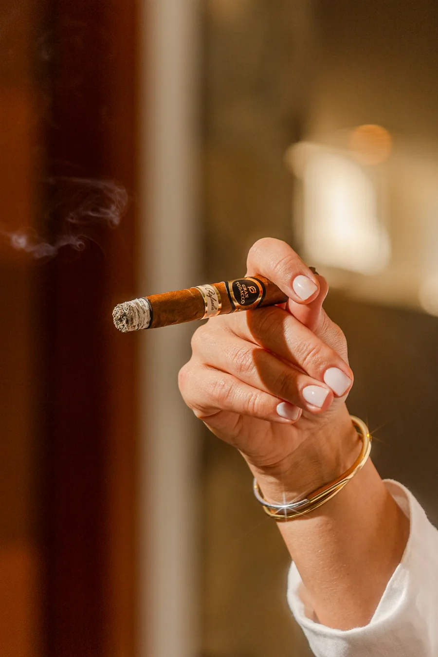 Mão feminina com pulseiras douradas segurando um charuto Gran Tobacco Rafaela aceso