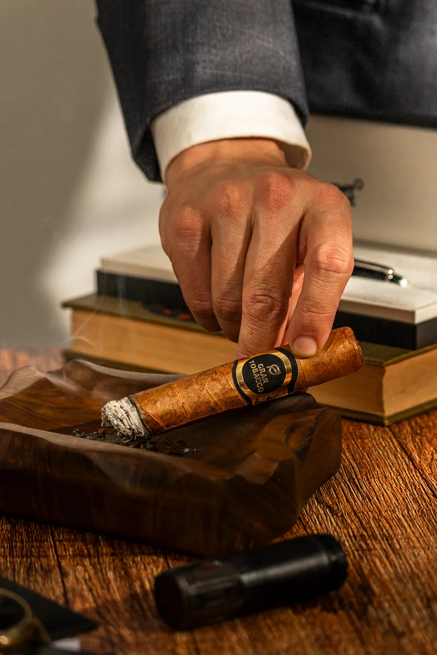 Mão de terno apoiando o charuto Gran Tobacco Robusto em um cinzeiro de madeira