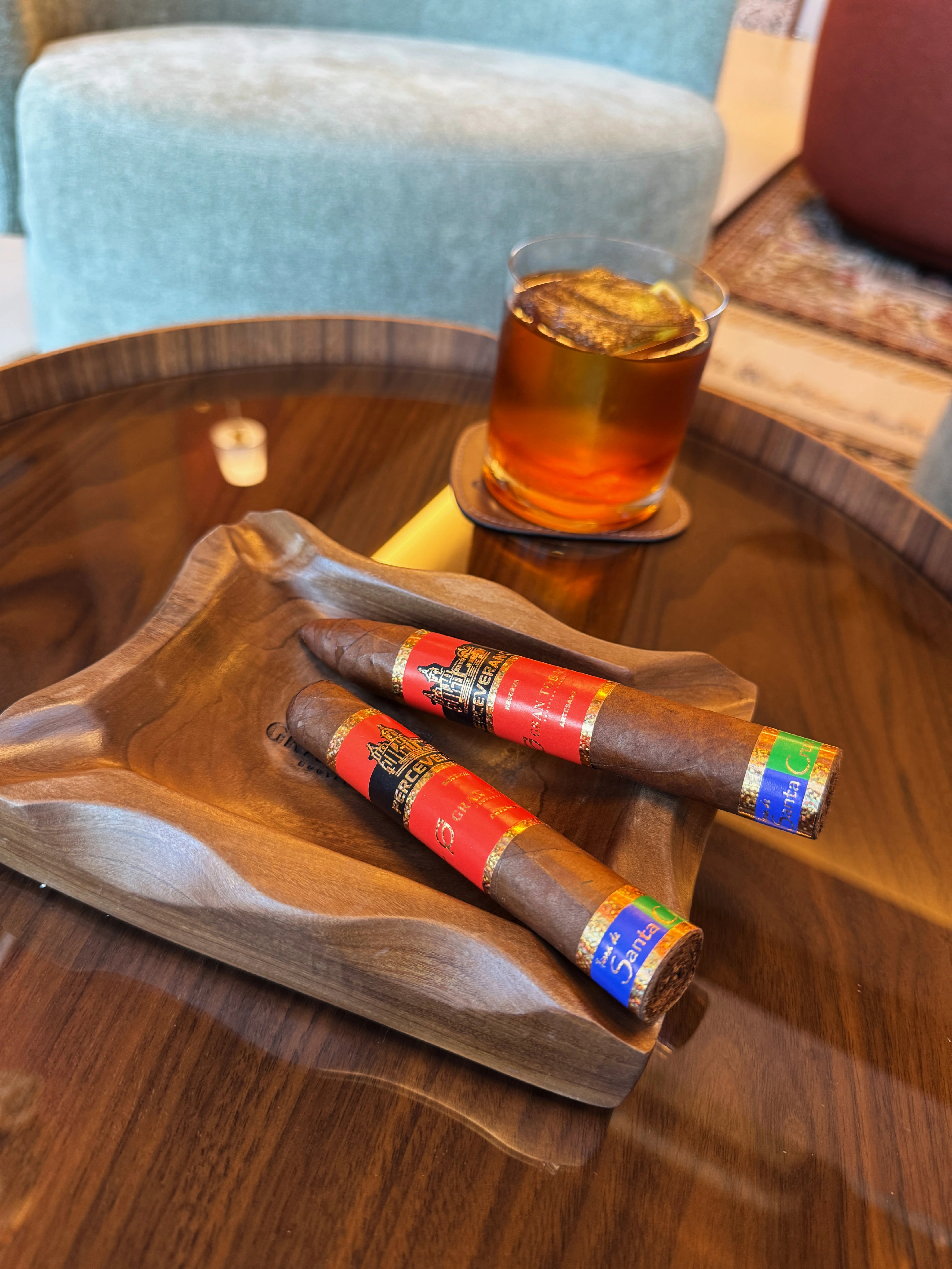 Dois charutos Terra de Santa Cruz em cinzeiro de madeira, ao lado de um copo de whisky